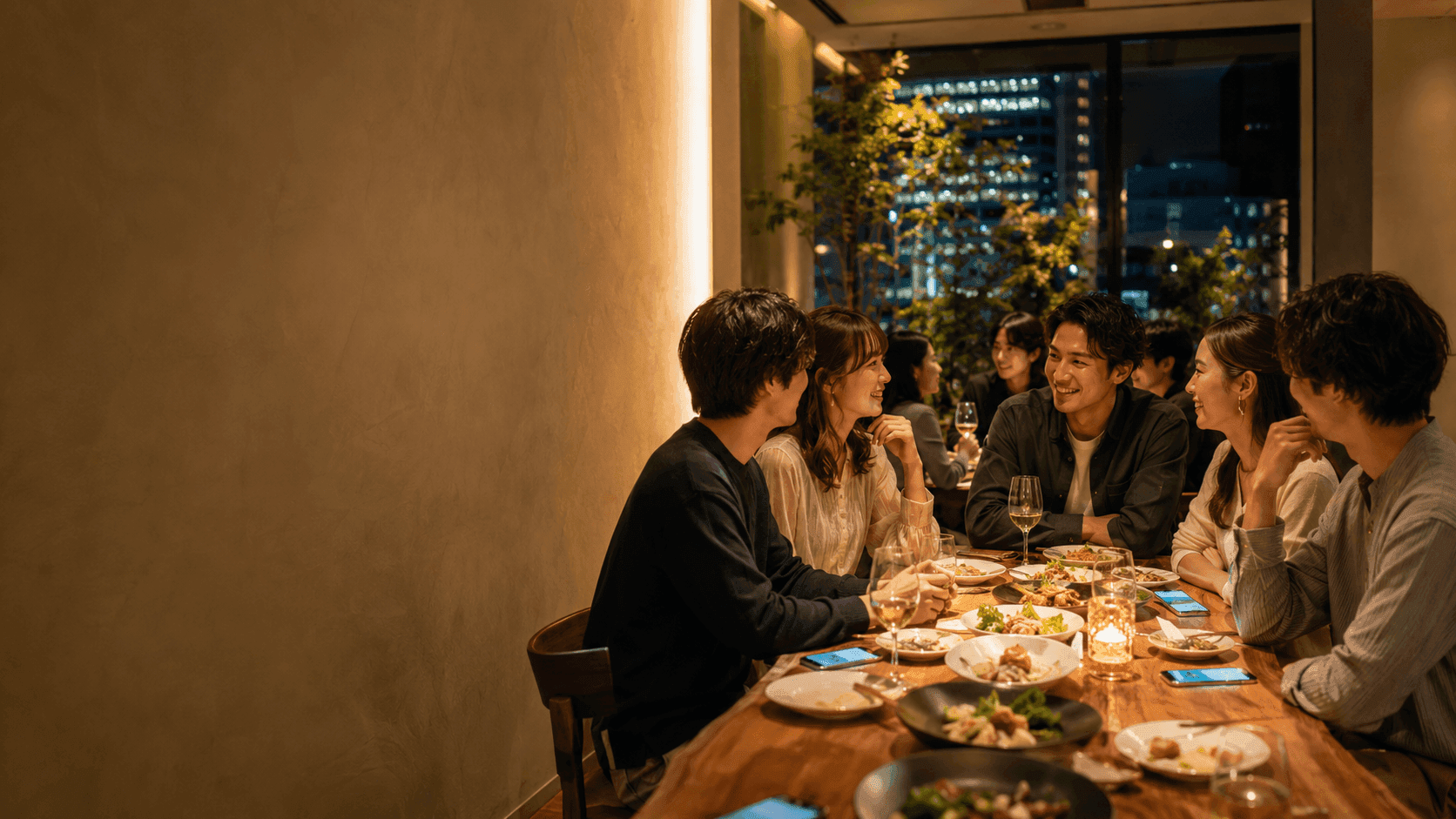 夜の店内で、テーブルを囲んで食事しながら談笑するグループ